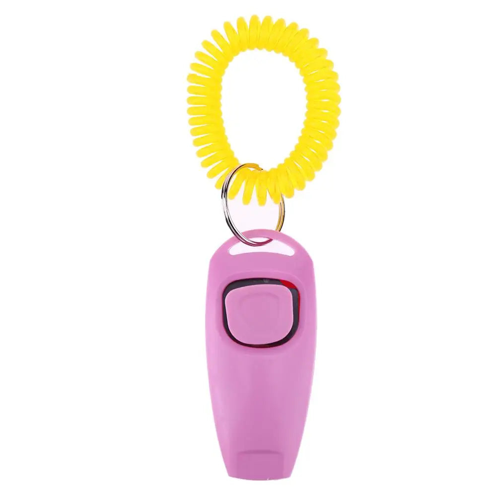 Clicker de dressage pour chiens de couleur rose posé sur un livre de couleur bleu. Le produit est sur une table de couleur claire. Image produit Boutiquechien