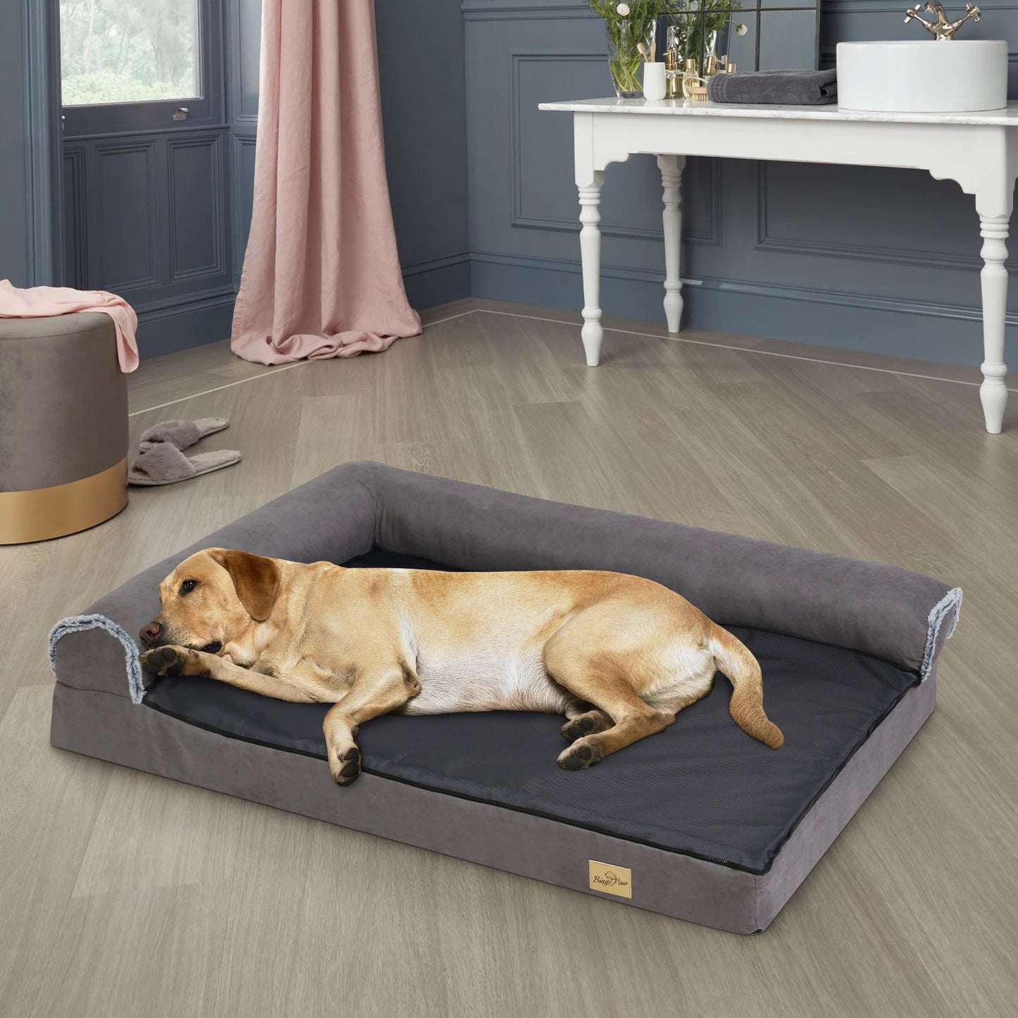 Tapis orthopédique pour chien de couleur gris. Le chien st de couleur blanc avec la tête posé sur son oreiller de couleur gris. Le chien est dans une maison avec sur les murs du noir et en fond une table blanche. Image produit Boutiquechien