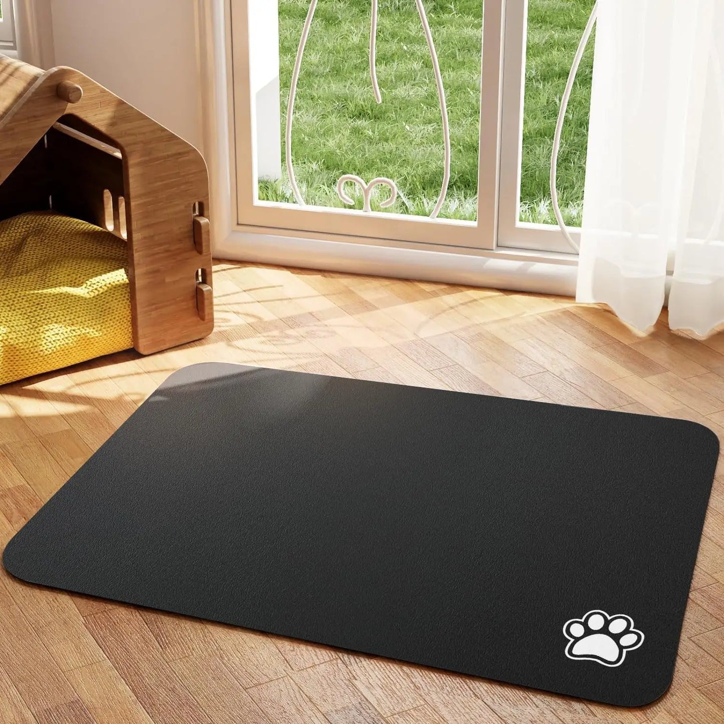 Tapis chien de couleur noir avec une patte de couleur blanche sur le tapis pour gamelle de chien. Le tapis à gamelle pour chien est posé dans un salon avec sur le côté une niche en bois. Image produit Boutiquechien