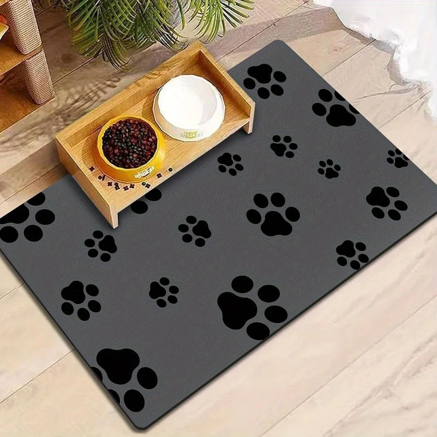 Tapis pour gamelle de couleur noir avec des formes de pattes dessus. Le tapis chien est résistant et durablea avec son caoutchouc. Elle est aussi posé dans une pièce de couleur claire avec en fond une plante verte. Image produit Boutiquechien