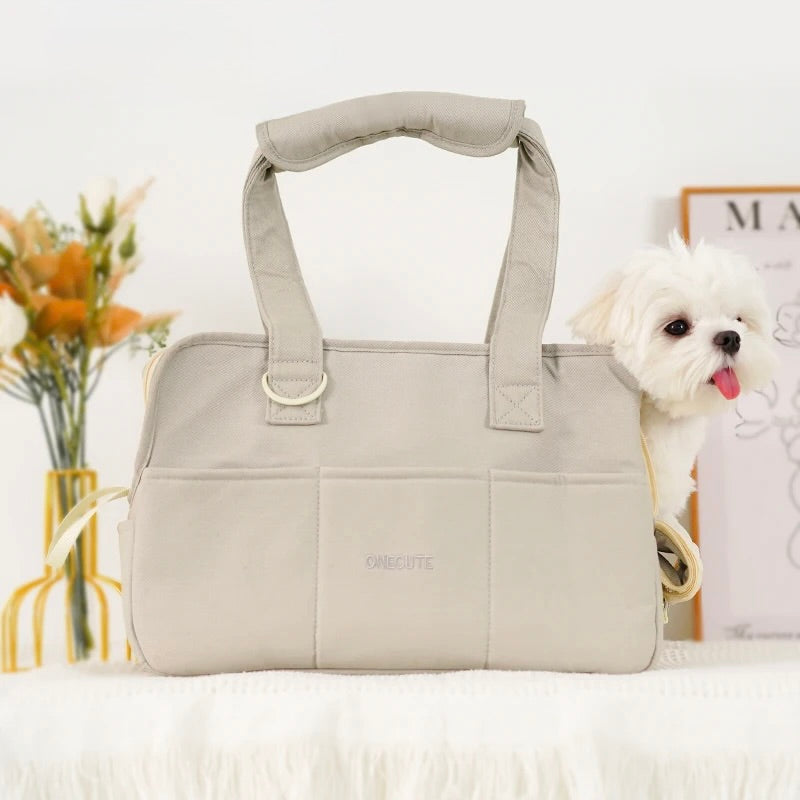 petit chien blanc dans un sac de couleur gris posé sur un canapé de couleur blanc avec en fond une plante verte et un tableau. Image produit Boutiquechien
