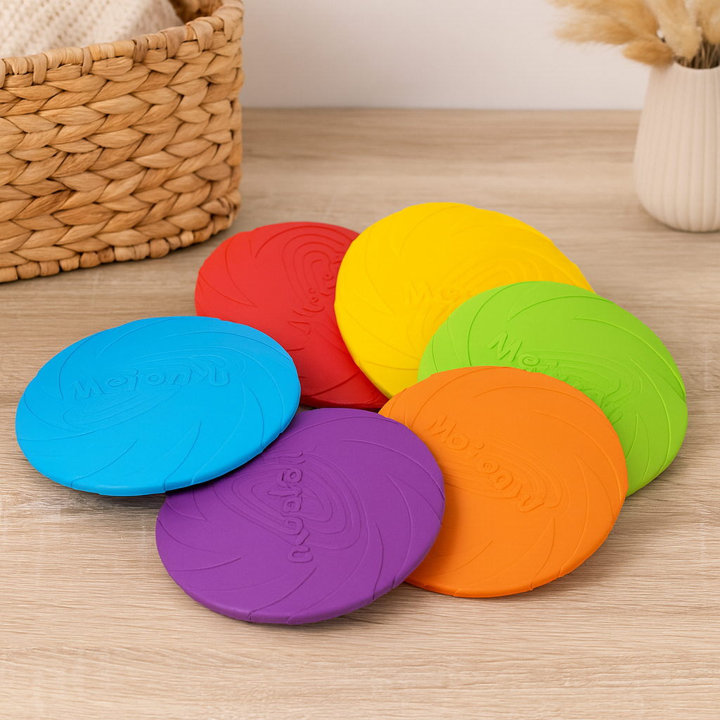Frisbee de couleurs différente pour les chiens avec en fond un panier en osier et une plante verte. Image produit Boutiquechien
