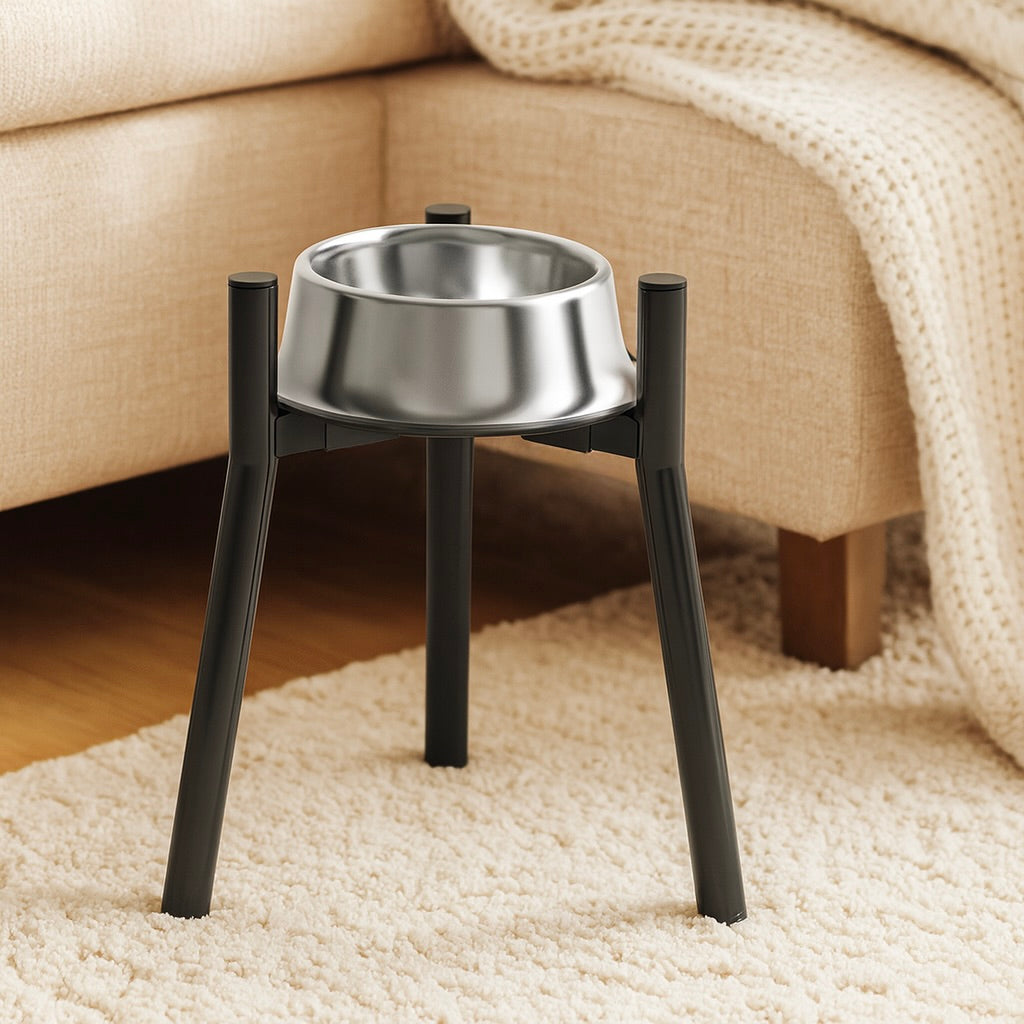 support de gamelle pour chein de couleur noir avec une gamelle en inox. En fond il y a un canapé de couleur gris sur un tapis blanc. Image produit Boutiquechien