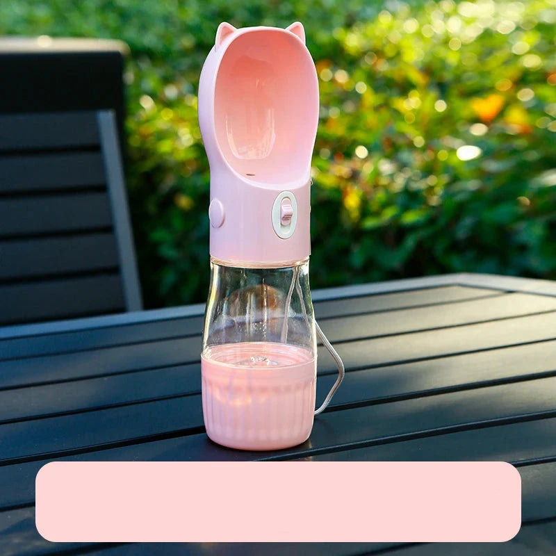 Gourde rose d'eau et nourriture posé sur une table de jardin de couleur noir avec en fond une haie verte. Image produit Boutiquechien