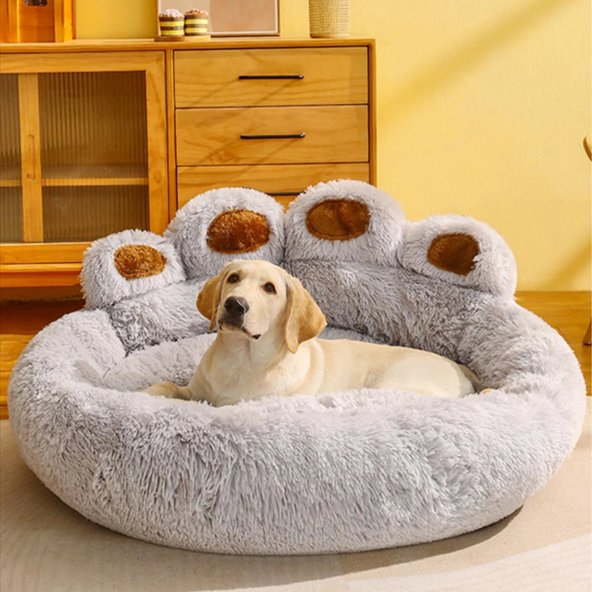 Golden retriever de couleur blanc de grande taille en dormant sur un panier chien de couleur gris. Le panier chien est posé dans un salon de couleur claire avec en fond un meuble en bois. Image produit Boutiquechien