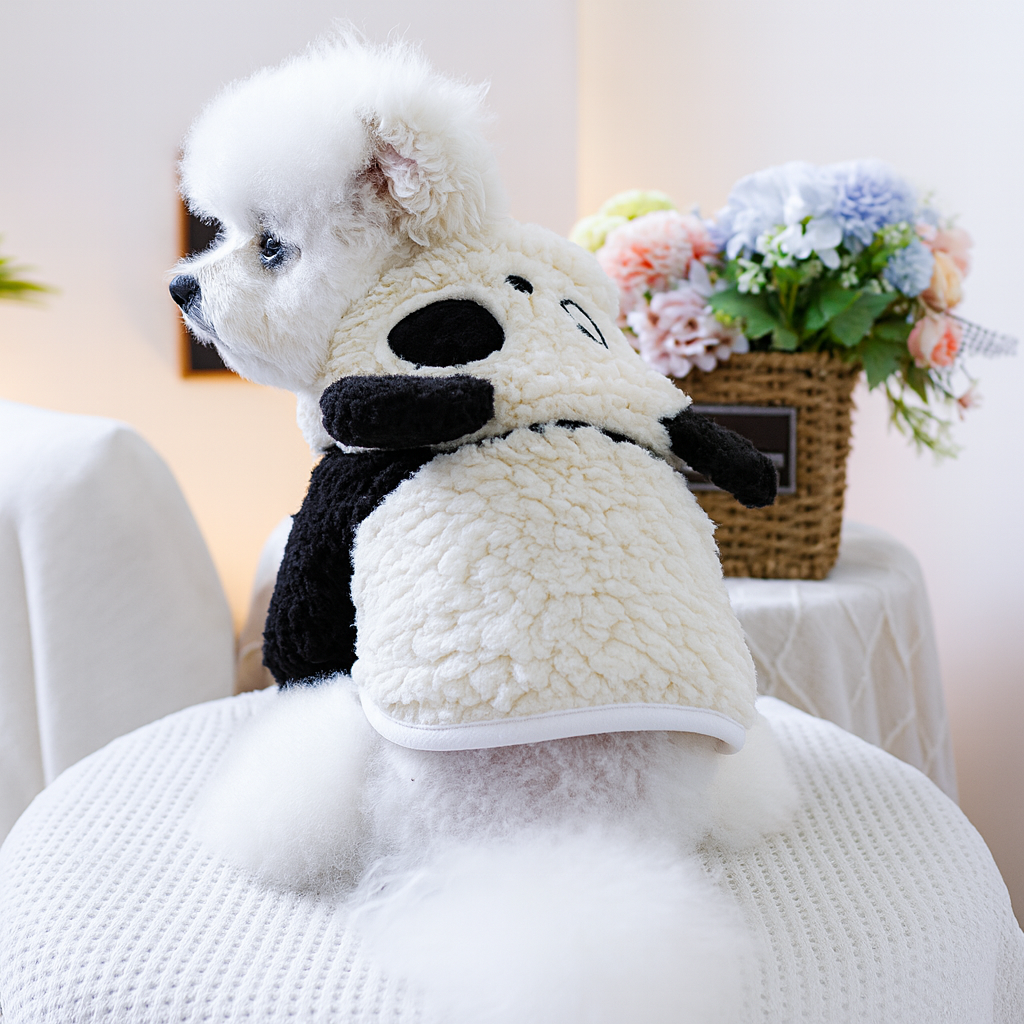Petit chien de couleur blanc portant un déguisement pour chien en forme de panda de couleur blanc et noir. Le chien porte une plante verte. Image produit Boutiquechien
