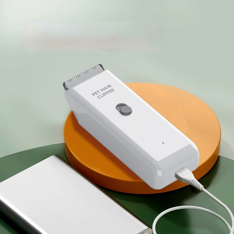Petite tondeuse de couleur blanc se faisant chargé par une batterie externe de couleur gris. Le produit est posé sur un socle de couleur orange. Image produit Boutiquechien