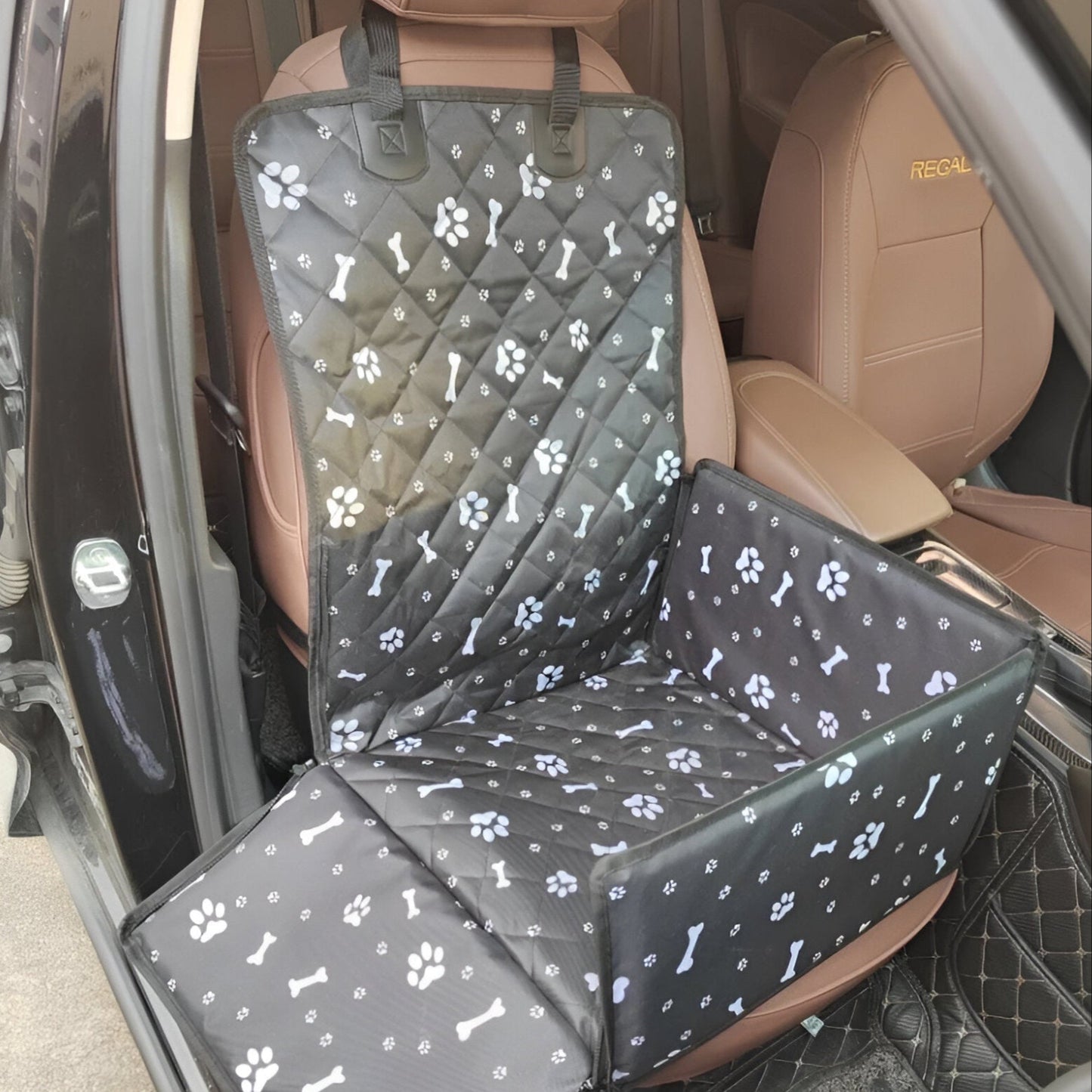 protection de siège pour voiture en forme de panier de couleur noir avec des formes de pattes et d'os blanc. La protection est posé sur un siège de couleur brun dans une voiture de couleur noir. Image produit Boutiquechien