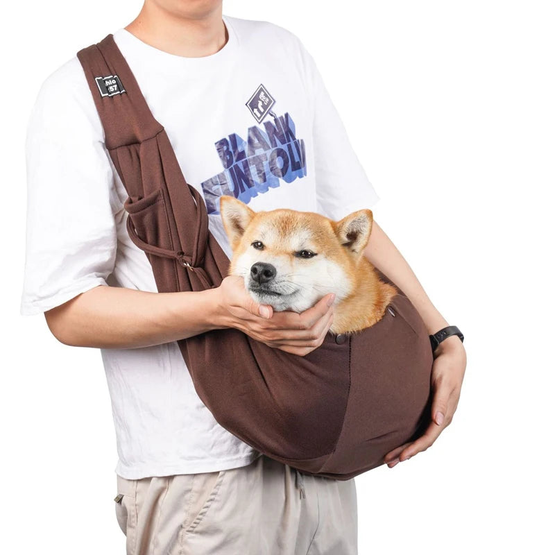 Sac pour chien brun porté par un homme habille en blanc avec un short claire. Le sac pour chien est de couleur noir avec une attache dans le sac. Image produit Boutiquechien