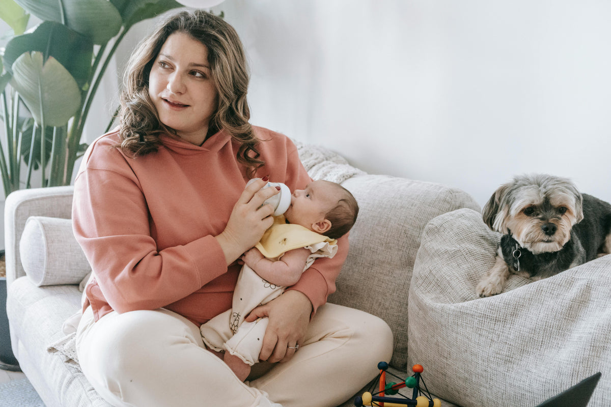 femme donnant du lait a son bebe avec un chien couchant a cote 