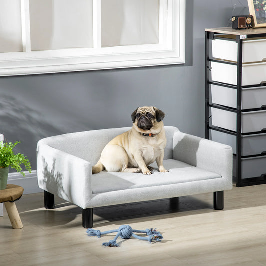 buldog de couleur blanc assis sur le canapé gris dans un salon claire. Image produit Boutiquechien