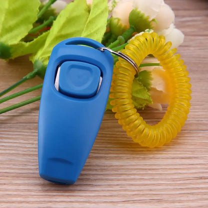 Clicker de dressage pour chiens de couleur bleu posé sur des fleurs. Le produit est sur une table de couleur claire. Image produit Boutiquechien