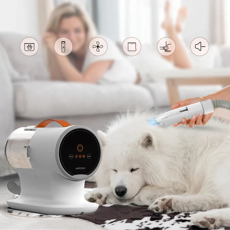 le pulseur pour chien de couleurs blanc avec poignée orange est utilisé sur un chien blanc de tailles tailles moyennes au grands poils. LE pulseur est utilisé dans un salon où en fond il y a une femme qui regarde sur un canapé 