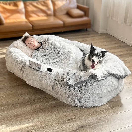 Panier homme et chien de couleur gris boutiquechien. Le panier chien est gris avec un chien blanc et gris. Une femme dors dans le panier chien. En fond il y a un canaoé cuir dans le salon. Image produit Boutiquechien