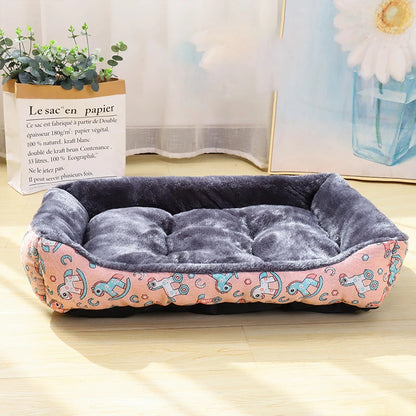Panier pour chien avec motif licorne dessus posé par terre à côté d'un tableau et d'un sac avec une plante verte dedans. Le panier à des licornes à bascules dessus 