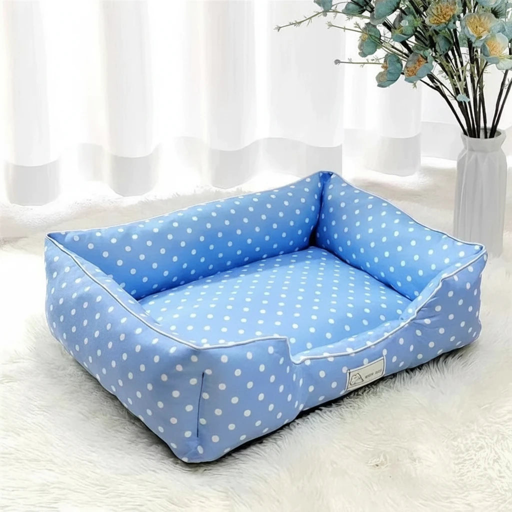 Panier pour petit chien a pois de couleur bleu et blanc dans un salon de couleur claire avec en fond une plante verte