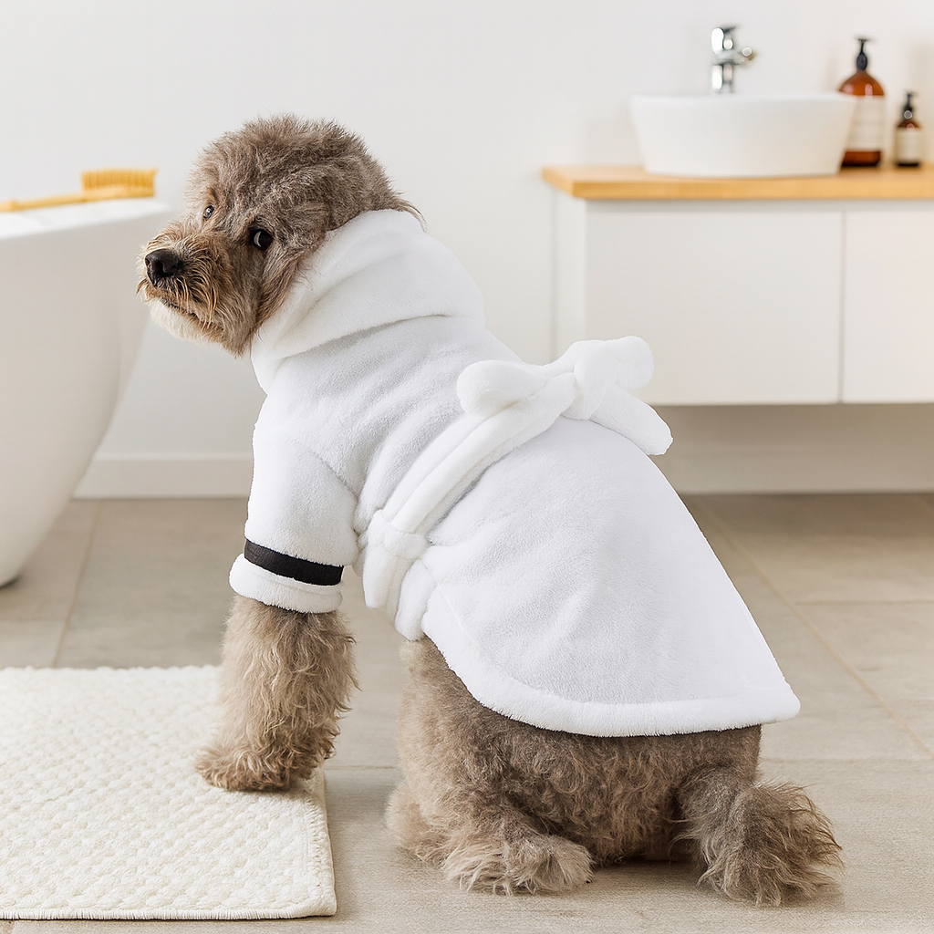 Peignoir pour chien de couleur blanc porté par un chien de taille moyenne gris. Le chien est mouillé car il est sorti de son bain qui est situé sur la gauche. Image produit Boutiquechien