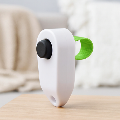 Clicker pour chien de couleur blancet noir avec attache verte. Le produit est mis en valeur dans un fond claire. Image produit Boutiquechien