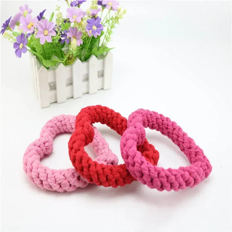 Jouet chien de couleurs rose et rouge posé dans un fond blanc près de fleur. Image produit Boutiquechien