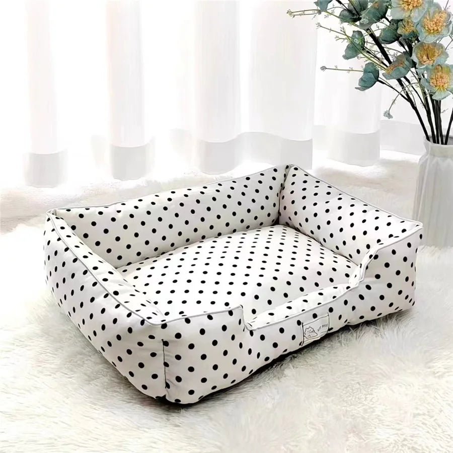 Panier pour petit chien a pois de couleur blanc et noir posé dans un salon de couleur claire avec des fleurs en fond