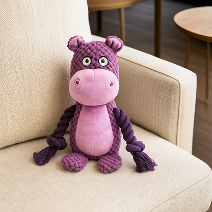 Peluche pour chien style corde positionné sur un canap gris. La peluche est un hippopotame de couleur violet dans un salon claire. Image produit Boutiquechien