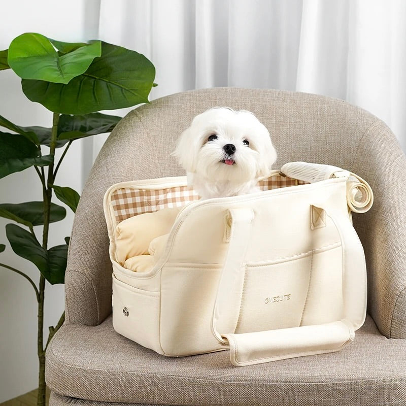 sac de transport pour chien de couleur blanc avec un petit chien de couleur blanc dedans moelleux. Le sac est posé sur un siège de couleur gris près d'une plante verte. Image produit Boutiquechien Image