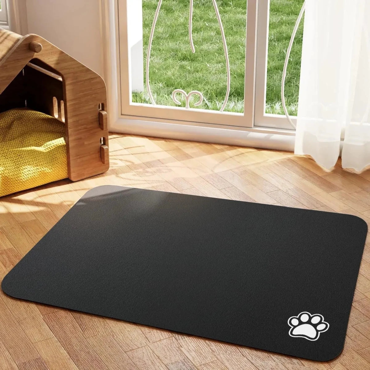 Tapis chien de couleur noir avec une patte de couleur blanche sur le tapis pour gamelle de chien. Le tapis à gamelle pour chien est posé dans un salon avec sur le côté une niche en bois. Image produit Boutiquechien