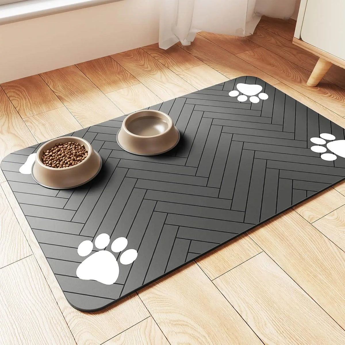 Tapis gamelle pour chien de couleur noir avec des formes de pattes de couleur blanc. Le tapis chien est posé dans un salon de couleur claire avec en fond un meuble blanc. La gamelle est posé sur le tapis gamelle chien. Image produit Boutiquechien Image